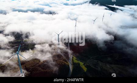 Luftaufnahme von einer Drohne eines Windparks über den Wolken und zwischen den Bergen. Stockfoto