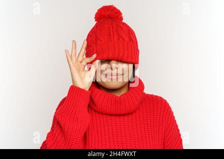 Verspielte lustige afrikanische Frau hat Spaß tragen Winterhut und Pullover decken Augen unter Mütze, Studio-Aufnahme Stockfoto