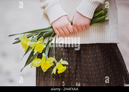 Kleines Mädchen in pastellfarbenen Kleidern mit gelben Narzissen, selektiver Fokus. Nahaufnahme, Hände Stockfoto