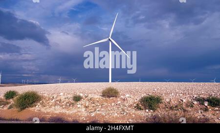 Bodenansicht einer Windturbine in der Mitte eines Windparks mit vielen Windturbinen im Hintergrund und dem bewölkten Himmel im Hintergrund Stockfoto