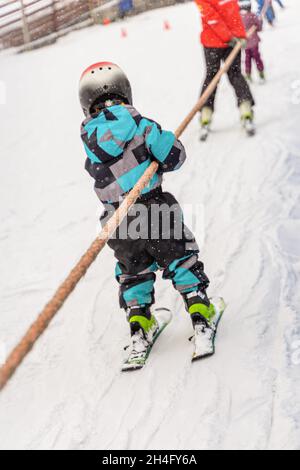 Kleines Kind auf Downhillskiern, das auf der Piste mit Surface Baby Lift auffährt. Winterurlaub, Sport-Lifestyle, Skikuruining und Outdoor-Familienurlaub Stockfoto