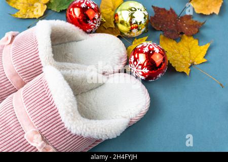 Warme und komfortable Hausschuhe mit gelben Blättern und Weihnachtsdekoration auf grünem Hintergrund. Rosa Farbe. Stockfoto