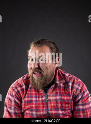 Lustiger Kerl mit langen Haaren und Bart, trägt kariertes Hemd winkend mit Auge im Studio Stockfoto