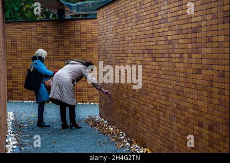 Amsterdam, Niederlande, 02/11/2021, zwei Frauen, die nach den Namen ihrer Angehörigen suchen, am Denkmal.70 Jahre nach dem Zweiten Weltkrieg haben mehr als 102,000 Opfer des Holocaust endlich ihr eigenes Denkmal. Dieses nationale Denkmal befindet sich im Herzen des jüdischen Viertels von Amsterdam. Das Denkmal besteht aus einem Labyrinth von Durchgängen, flankiert von zwei Meter hohen Ziegelwänden, die die Botschaft ‘in Erinnerung an' vermitteln. Auf jedem der Ziegel ist der Name jedes Holocaust-Opfers eingeschrieben. Die meisten Menschen, die das Denkmal besuchen, halten Papiere mit den Namen ihrer lo Stockfoto