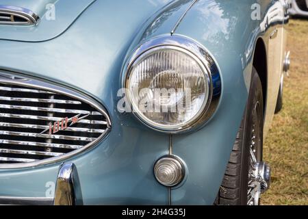 Nahaufnahme des Scheinwerfers und des Kühlergrills vorne links auf einem silberblauen Austin-Healey 100-6 British 1950er Open Top-Sportwagen Stockfoto