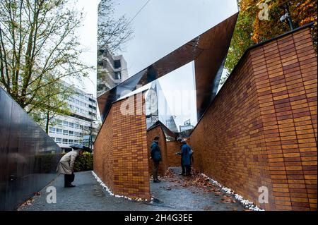 Menschen vor Ort besuchen das Denkmal siebzig Jahre nach dem Zweiten Weltkrieg haben mehr als 102,000 Opfer des Holocaust endlich ihr eigenes Denkmal. Dieses nationale Denkmal befindet sich im Herzen des jüdischen Viertels von Amsterdam. Das Denkmal besteht aus einem Labyrinth von Durchgängen, flankiert von zwei Meter hohen Ziegelwänden, die die Botschaft ‘in Erinnerung an' vermitteln. Auf jedem der Ziegel ist der Name jedes Holocaust-Opfers eingeschrieben. Die meisten Menschen, die das Denkmal besuchen, halten Papiere mit den Namen ihrer Angehörigen, die sie während des Zweiten Weltkriegs verloren haben, um die Steine mit zu finden Stockfoto