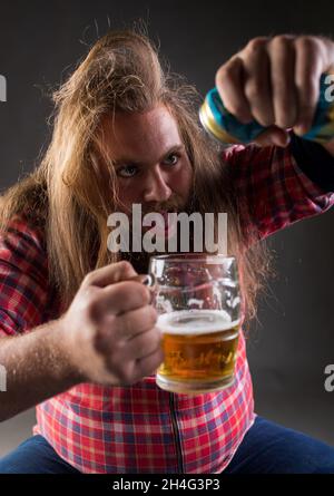 Chaotisch betrunkener Mann, der im Studio Bier aus der Dose in den Becher gießt Stockfoto