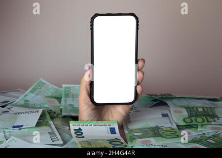 Konzept der Arbeit mit dem Telefon, um mit dem Telefon zu arbeiten. Hand mit einem Telefon kriecht aus einem Haufen Geld Stockfoto