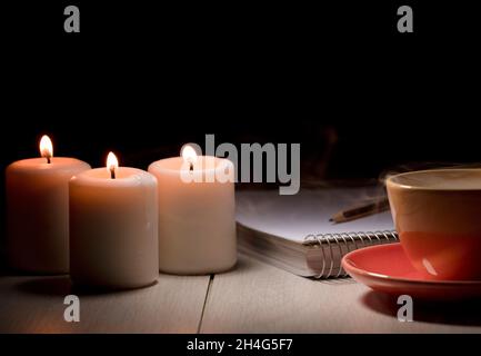 Tisch mit brennenden Kerzen Bleistiftheft, gelber Becher mit Rauchdampf. Stockfoto