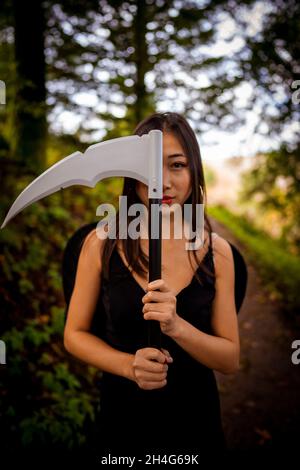 Junge Frau mit einem Cosplay-Outfit für den Sensenmann im Wald Stockfoto