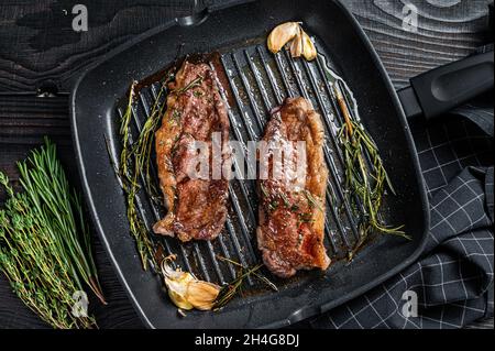 Gegrillte Prime Black Angus Rindersteaks Striploin oder New York in einer Grillpfanne. Dunkler Holzhintergrund. Draufsicht Stockfoto