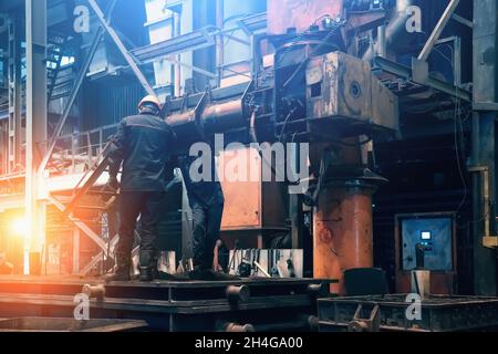 Innen des Stahlwerks. Die Arbeiter in der Werkstatt der metallurgischen Anlage. Gebäude der Gießerei und der Schwerindustrie im Hintergrund.