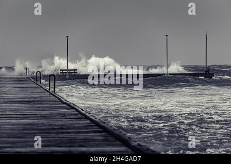 Wellen krachen an einem düsteren, stürmischen Tag in Schwarz und Weiß über dem Frankston Pier Stockfoto