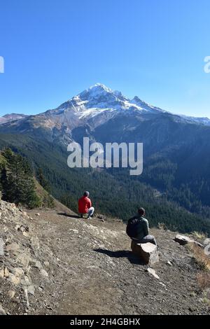 Zwei Wanderer genießen an einem Oktobertag auf dem McNeil Point Trail in der Mt Hood Wilderness, Oregon, USA, eine spektakuläre Aussicht auf Mt Hood vom bald Mountain. Stockfoto