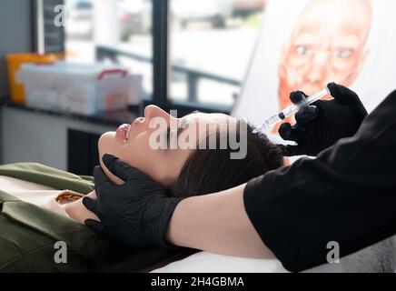 Junge Frau mit Haarproblemen, die in einer Klinik Injektionen in die Kopfhaut erhalten. Mesotherapie Behandlung von Haarausfall, Injektion für das Haarwachstum Stockfoto