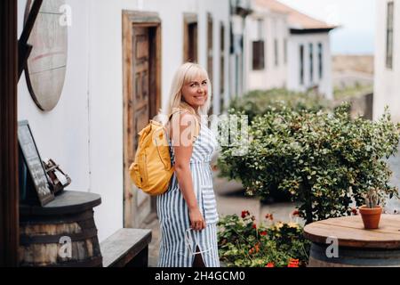 Eine Blondine in einer Sundress mit einem Rucksack geht entlang der Straße der Altstadt von Garachico auf der Insel Teneriffa.Spanien, Kanarische Inseln Stockfoto