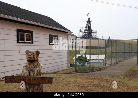 Die Ansicht eines Kopfgestells über dem Minenschacht von einer Wohnstraße mit einer hölzernen Bierstatue davor.Butte.Montana.USA Stockfoto