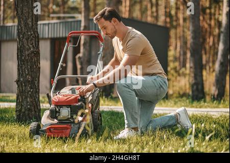 Mann hockend in der Nähe des Rasenmähers im Freien Stockfoto