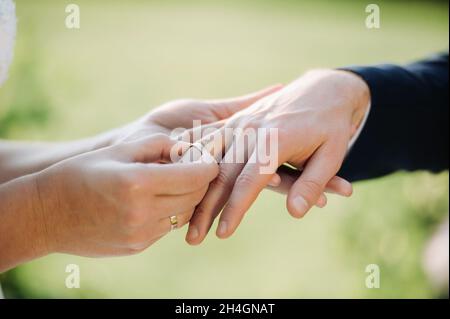 Am Hochzeitstag legt die Braut einen Verlobungsring auf den Finger des Bräutigams. Stockfoto