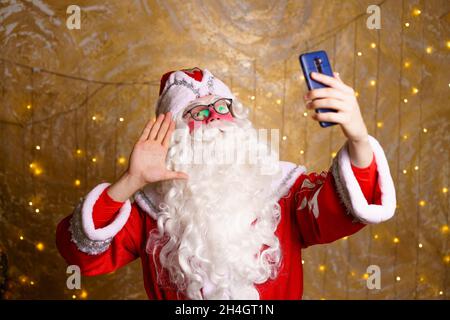 Der weihnachtsmann nimmt während der weihnachtszeit mit dem Mobiltelefon Selfie auf oder kommuniziert per Videokommunikation. Ein luxuriöses weihnachtsgeschenk oder ein Geschenk für gutes Benehmen. Neues Jahr. Stockfoto