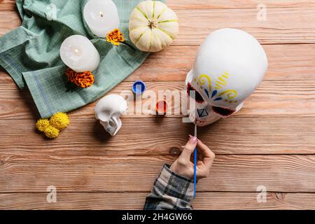 Frau, die menschlichen Schädel auf hölzernen Hintergrund malt. Mexikos Tag der Toten (El Dia de Muertos) Stockfoto