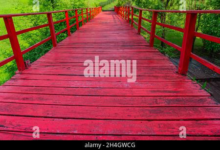 Perspektivische Ansicht der rot gealterten Holzbrücke in einem Garten, alte Holzbrücke, keine Menschen. Stockfoto