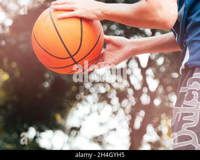 Ein Teenager, der einen Basketball hält, bereitet sich darauf vor, den Ball auf dem Platz im Freien in den Reifen zu werfen. Stockfoto