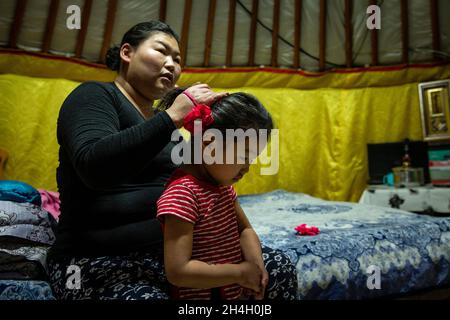 Pagmadulam, 33, bindet die Haare ihrer Tochter Khngorzul, 4, in ihrem Haus, als sich die Nacht in einem Ger-Bezirk der Hauptstadt Ulaanbaatar nähert, Januar 19 Stockfoto