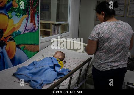 Eine Mutter schaut in einer Kindernotaufnahme in einem der städtischen Krankenhäuser in der Hauptstadt auf ihren kleinen Jungen, der an Atemwegserkrankungen leidet Stockfoto