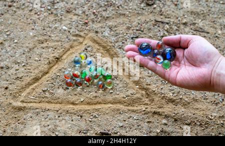 Die Hand eines Mannes, der Murmeln auf einem Spielplatz mit Schmutz spielt. Stockfoto