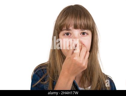 Kleines Mädchen in kariertem braunem Hemd, das sich wegen des schlechten Geruchs in die Nase kneift. Sie ist unzufrieden mit Gestank und Blick auf die Kamera. Stockfoto