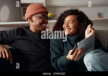 Multiethnisches Paar freut sich über Online-Einkäufe, die mit einem Tablet auf dem Sofa in der Lounge getätigt werden Stockfoto