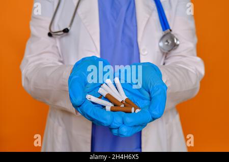 Ärztin hält gebrochene Zigaretten mit Tabak in den Händen, roter Studiohintergrund Stockfoto