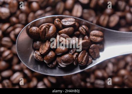 Dunkel geröstete Arabica-Kaffeebohnen in einem Edelstahllöffel. Stockfoto