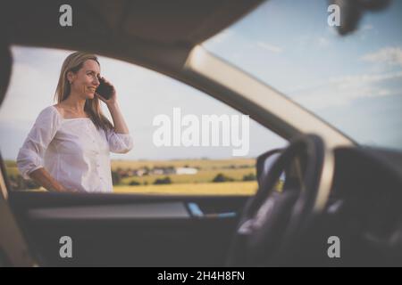 Hübsche Frau im mittleren Alter am Steuer ihres Autos, eine Pause auf einer langen Reise, einen Anruf zu machen Stockfoto