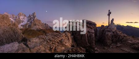 Gipfelkreuz und Jesusfigur auf dem Monte Castellaz, Sonnenuntergang, im Hintergrund Pala Group, Cimon della Pala, Parco Naturale Paneveggio Pale di San Stockfoto