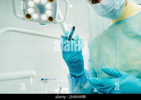 Ein maskierter Zahnarzt hält eine Injektionsspritze für einen Patienten im Büro. Stockfoto