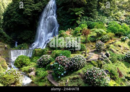 Eine Touristenfrau schaut auf die Kaskaden eines Ribeira dos Caldeirões Wasserfalls auf der Insel Sao Miguel auf den Azoren, Portugal Stockfoto