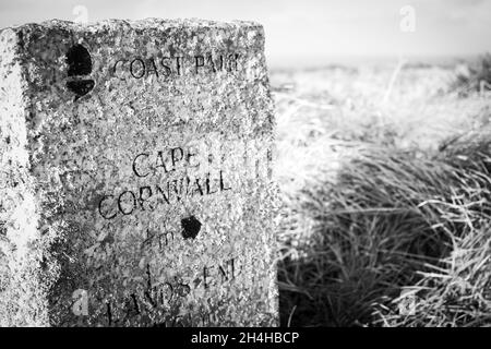 Nahaufnahme eines Wandermarkers aus Stein, der in Richtung Cape Cornwall auf dem South West Coast Path, Großbritannien, zeigt, schwarz-weiß Stockfoto