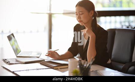 Nachdenkliche Geschäftsfrau, die über Werke nachdenkt, nachdenkliche Geschäftsfrau, die an finanziellen Informationen arbeitet, während sie ein Tablet verwendet. Stockfoto