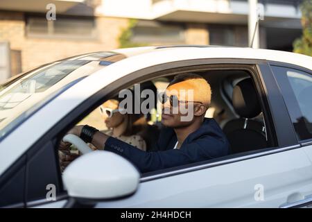 Glückliches multirassisches Paar, das zusammen am Auto fährt Stockfoto