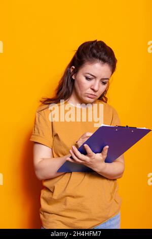 Junge Person, die im Studio Notizen zu Notizbuchdateien mit Stift gemacht hat. Konzentrierte Frau, die auf Lehrbuchpapieren schreibt, Dokumente unterschreibt und Papierkram über Projekt auf Notizblock-Zwischenablage. Stockfoto