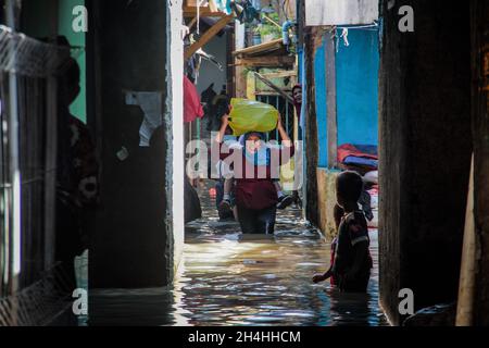 Dayeuhkolot, Indonesien. November 2021. Eine Frau, die ihre Habseligkeiten trägt, wurde in einem überfluteten Gebiet gesehen. Der Citarum-Fluss überlief aufgrund der starken Regenfälle, die Tausende von Häusern in Bandung, darunter Dayeuhkolot, Bojongsoang und Baleendah, überschwemmten. (Foto von Algi Febri Sugita/SOPA Images/Sipa USA) Quelle: SIPA USA/Alamy Live News Stockfoto