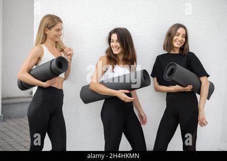 Mädchen stehen mit Fitnessmatten und unterhalten sich im Freien Stockfoto