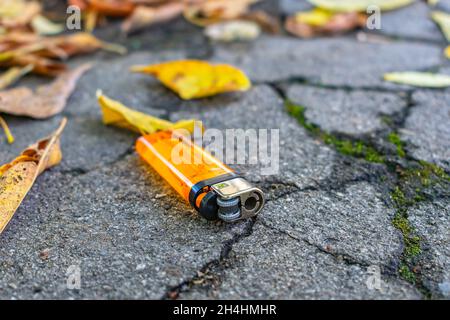 Verlorenes orangefarbenes Taschenfeuerzeug liegt auf der Straße zwischen herbstlichen Blättern Stockfoto