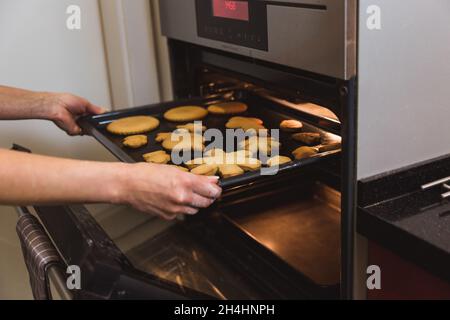 Seitenansicht der Hände einer Frau, die das Gericht aus dem Ofen in der Küche herauszieht. Frau backen Lebkuchengebäck Stockfoto