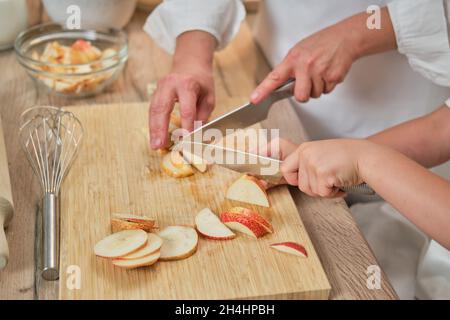 Mutter und Sohn in weißen Chefkleidern schnitten in ihrer eigenen Küche mit einem Messer Birnen. Eine Erwachsene Frau mit einem kleinen Jungen wird einen Kuchen kochen Stockfoto