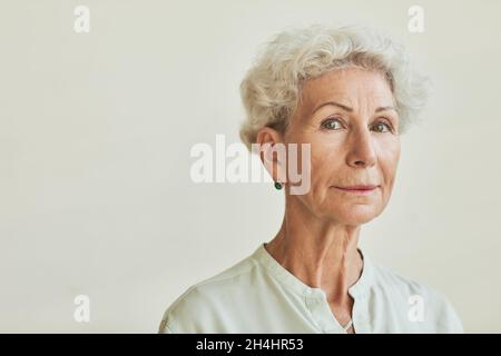 Nahaufnahme des Porträts einer eleganten älteren Frau, die vor neutralem Hintergrund auf die Kamera schaut, und des Kopierbereichs Stockfoto