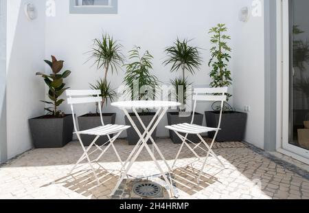 Innenhof mit weißem Metalltisch, Stühlen und Pflanzgefäßen