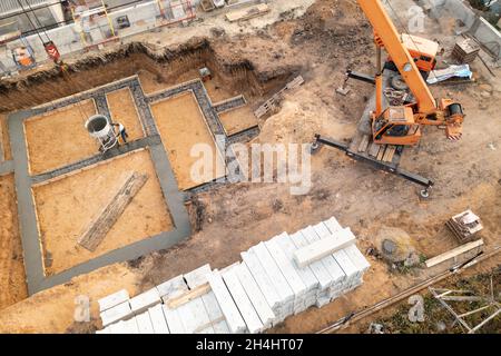 Gründung eines zukünftigen Hauses. Gießfundament mit Zement auf Baustelle mit Kran, Luftaufnahme. Stockfoto